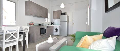 A compact living space with a kitchenette, a dining area, and a green sofa with cushions.