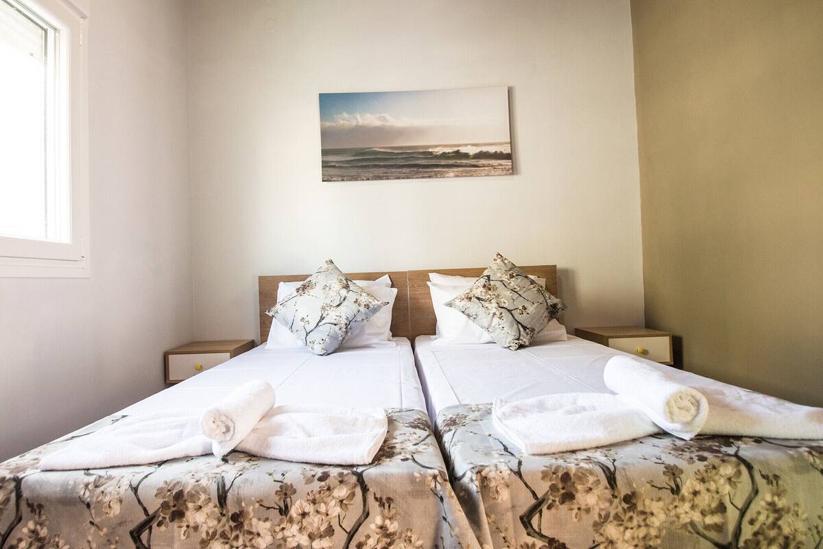 Ein Doppelbett mit Blumenmuster auf der Bettwäsche, zwei Kissen und aufgerollte Handtücher.
