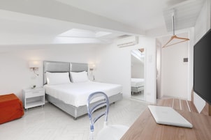 Un dormitorio moderno con cama, mesitas de noche, un escritorio con una computadora portátil, un espejo y un aire acondicionado.