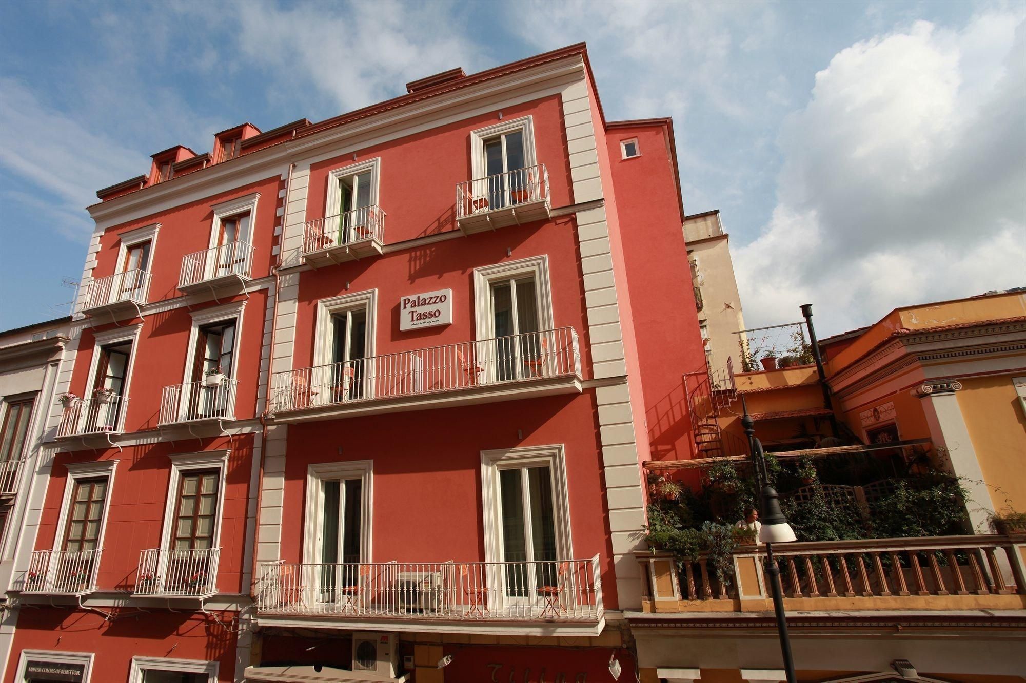 A multi-story building with balconies, a sign reading "Palazzo Tasso," and a clear sky.