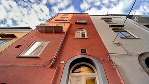 A building with a red facade, a central arched entrance, and multiple windows. - Palazzo La Via - One Bedroom (Massa Lubrense)