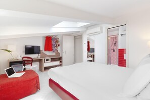 Una habitación de hotel moderna con cama, escritorio, televisor y zona de ducha.