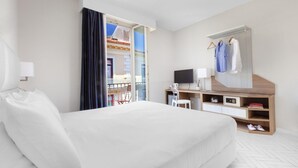 Ein Hotelzimmer mit einem großen Bett, einem Schreibtisch mit Computer, einem Fernseher und einem Kleiderschrank mit Kleidung.