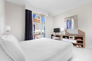 Ein Hotelzimmer mit einem großen Bett, einem Schreibtisch mit Computer, einem Fernseher und einem Kleiderschrank mit Kleidung.