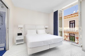 Ein Hotelzimmer mit einem großen Bett, einem Nachttisch mit Lampe, einem kleinen Schreibtisch mit Computer und einer Schiebetür zum Balkon.