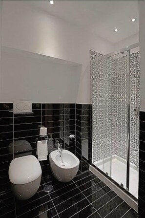 Ein modernes Badezimmer mit schwarzem Fliesenboden, Toilette, Bidet und Dusche mit Glastür.