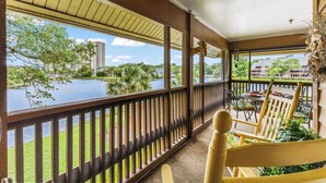 A covered balcony with a view of a lake, outdoor seating, and a giraffe decoration.