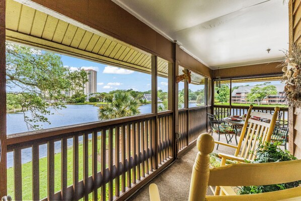 A covered balcony with a view of a lake, outdoor seating, and a giraffe decoration.