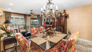 A dining area with a glass-top table, red floral chairs, a chandelier, and a decorative centerpiece.