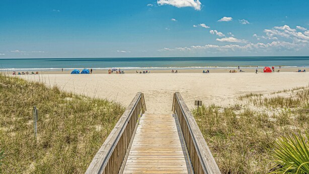 A wooden boardwalk leading to a beach with tents and people.