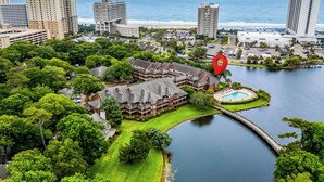 An aerial view of a resort with a swimming pool, a bridge over water, and a view of the ocean.