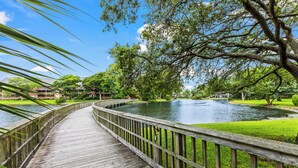 A wooden boardwalk with a metal railing, leading to a body of water surrounded by greenery and trees.