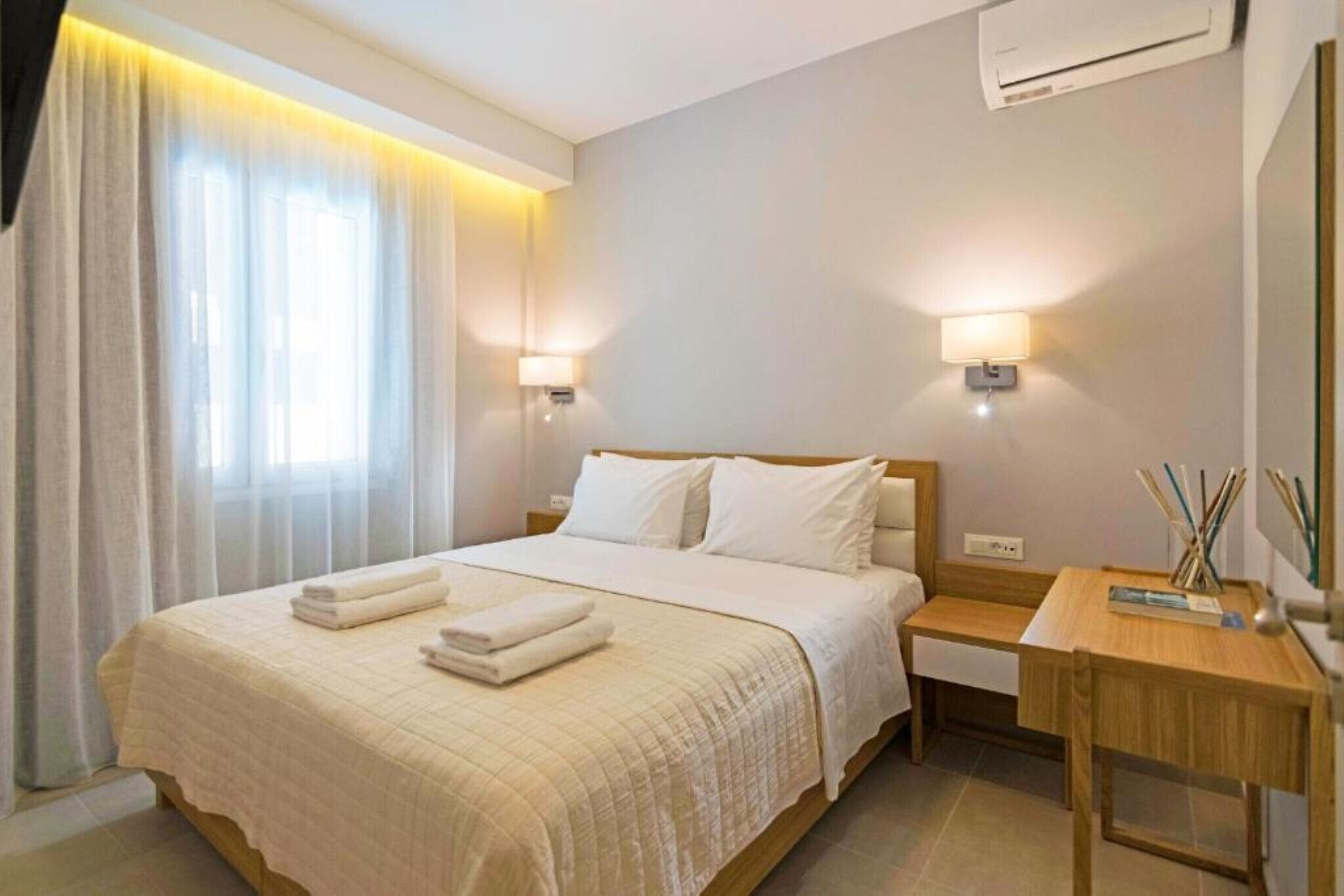 Een hotelkamer met een groot bed, twee nachtkastjes, een bureau en een raam met gordijnen.