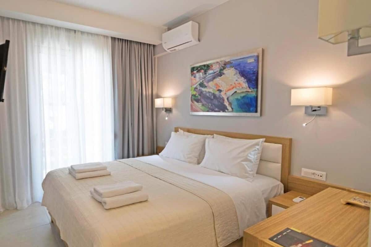 A hotel room with a bed, bedside lamps, a painting on the wall, and a window with curtains.