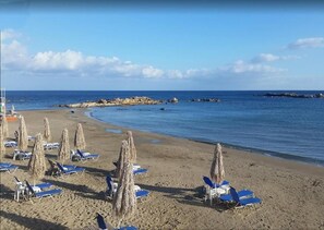 Une plage avec des transats et des parasols, un ciel dégagé et une mer calme.