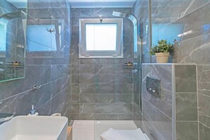 Une salle de bain moderne avec une baignoire, une douche et une petite fenêtre.