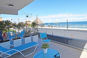 Un balcon avec des fauteuils de jardin bleus, des plantes en pot et une petite table sur laquelle sont posées des lunettes de soleil.