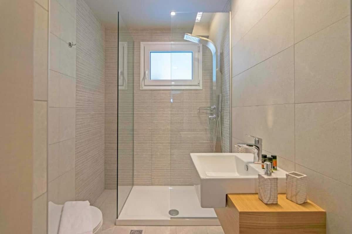 A modern bathroom with a glass-enclosed shower, a built-in sink, and a small window.