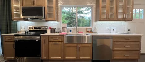 A modern kitchen with wooden cabinets, stainless steel appliances, and a large window providing natural light.