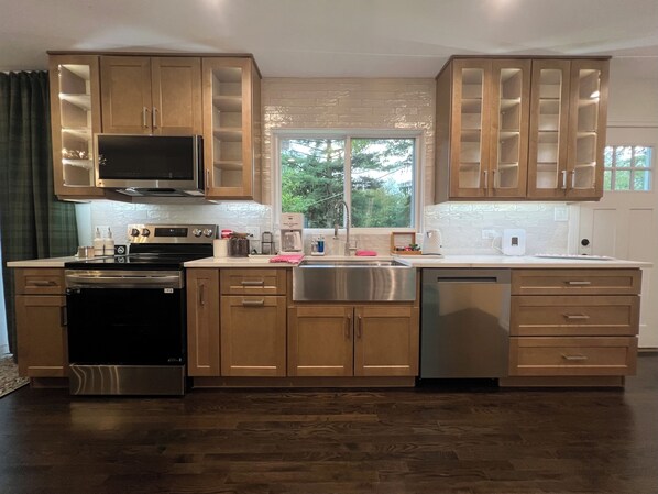 A modern kitchen with wooden cabinets, stainless steel appliances, and a large window providing natural light.