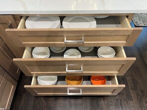 A kitchen drawer with multiple compartments, each containing white plates and bowls.