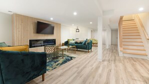 A modern living room with a flat-screen TV, a green sofa, a wooden accent wall, and a staircase. - Elegant Escape by Downtown Burr Ridge with an easy access to Chicago Landmarks (La Grange)