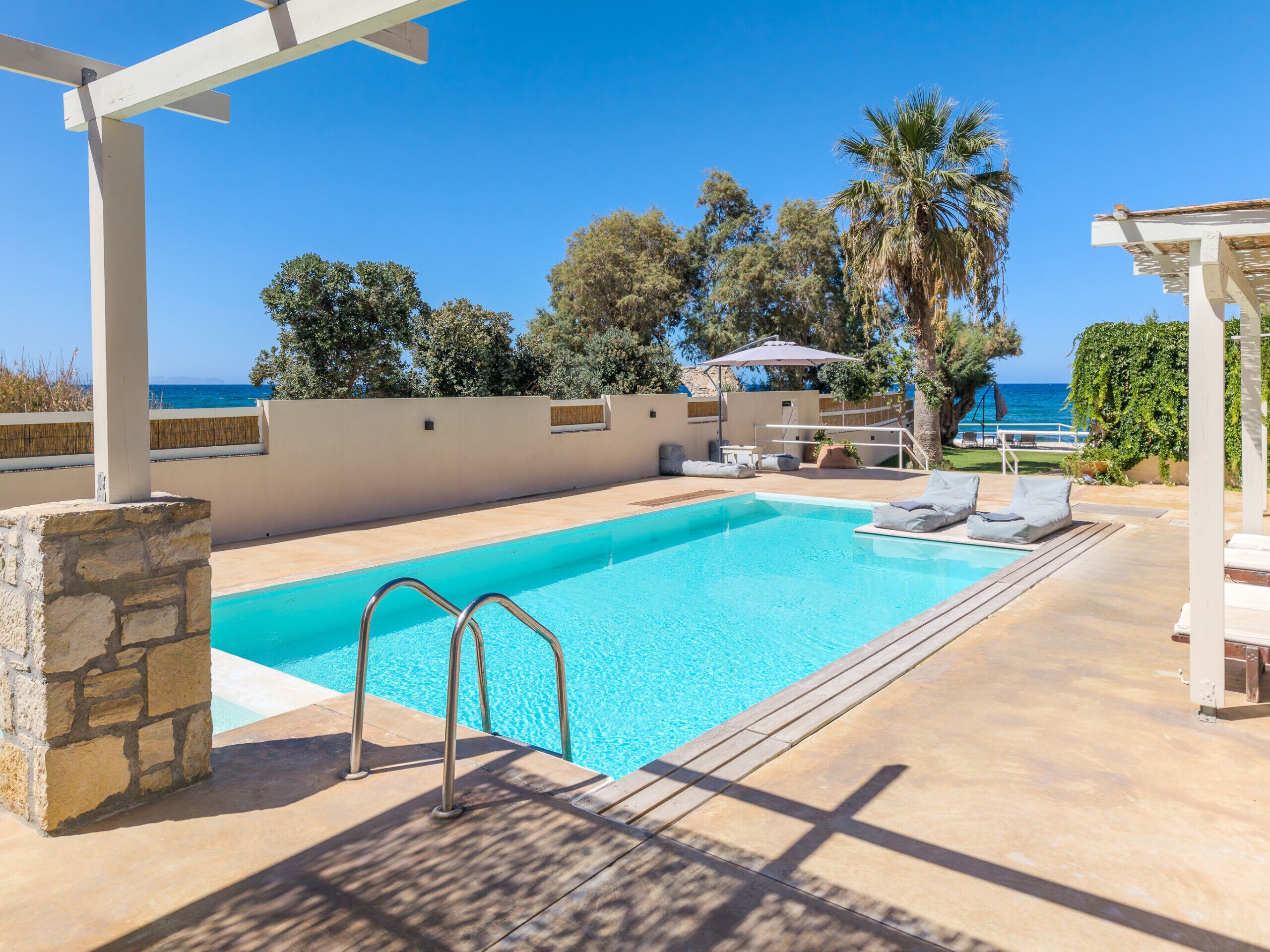 A swimming pool with a view of the sea, surrounded by lounge chairs and a pergola.