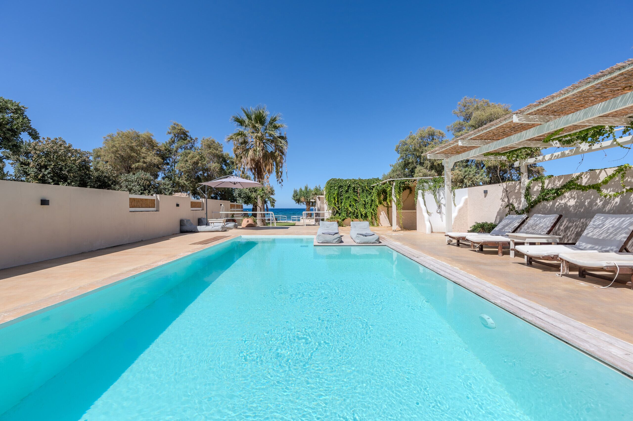 A swimming pool with lounge chairs and umbrellas, surrounded by trees and a view of the sea.