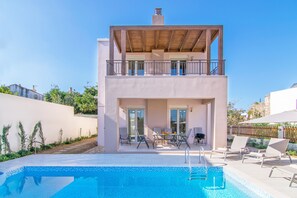 Une maison moderne à deux étages dotée d’une piscine, d’un espace salon extérieur et d’un balcon.