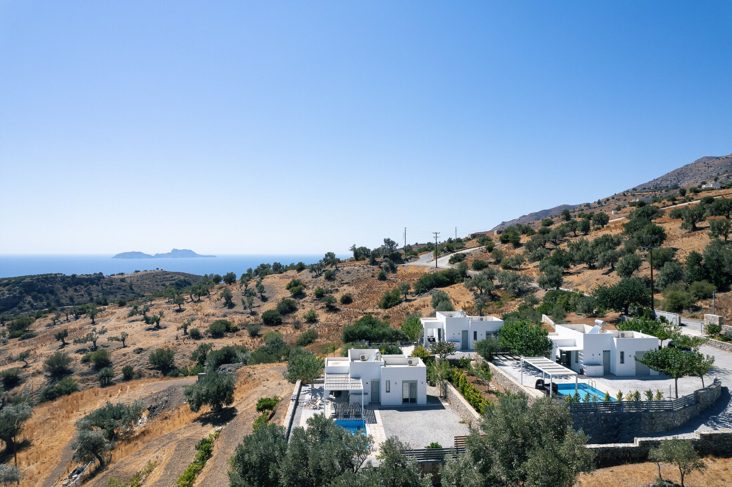 A coastal property with white buildings, a swimming pool, and a view of the sea and hills.