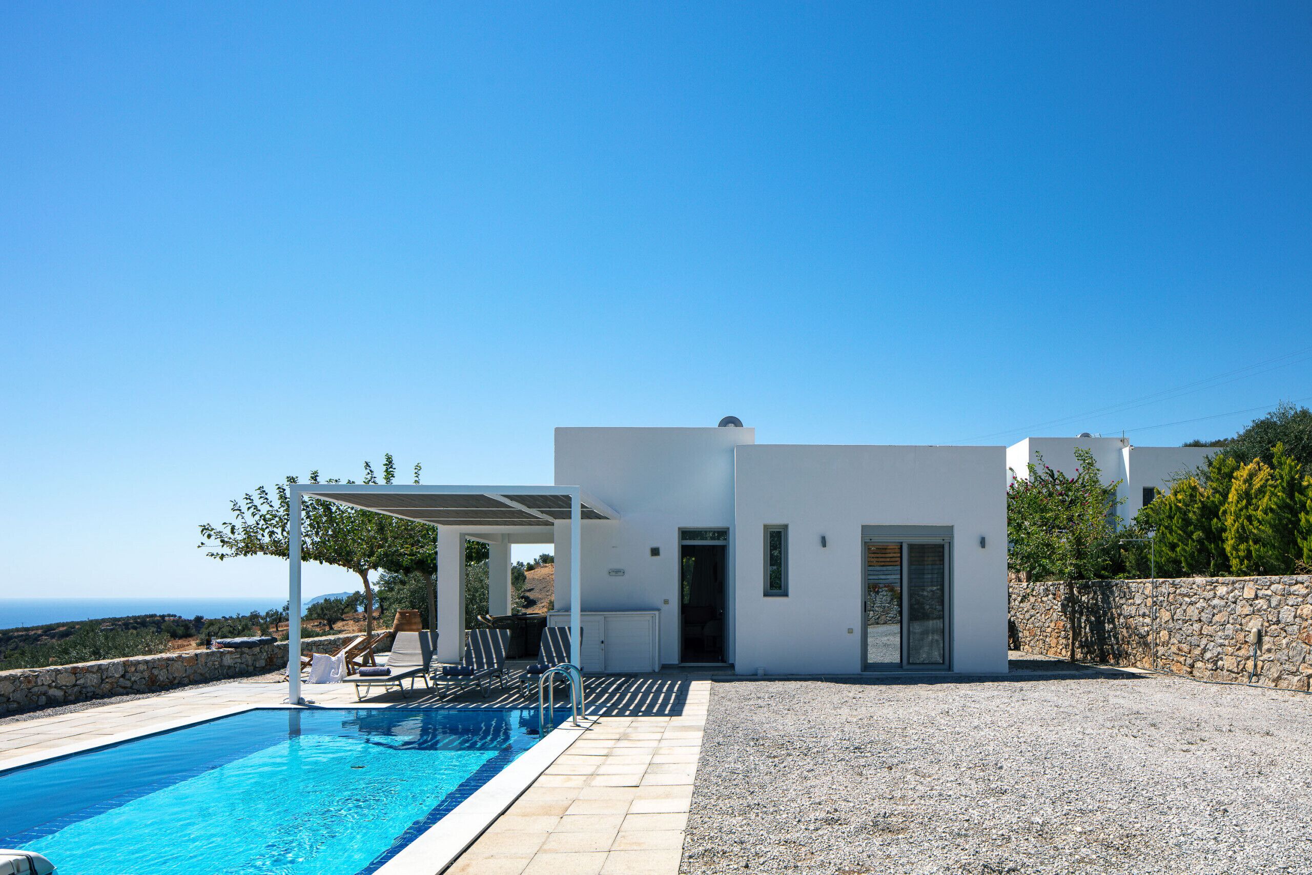 A modern villa with a swimming pool, outdoor seating, and a view of the sea.