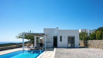 A modern villa with a swimming pool, outdoor seating, and a view of the sea.