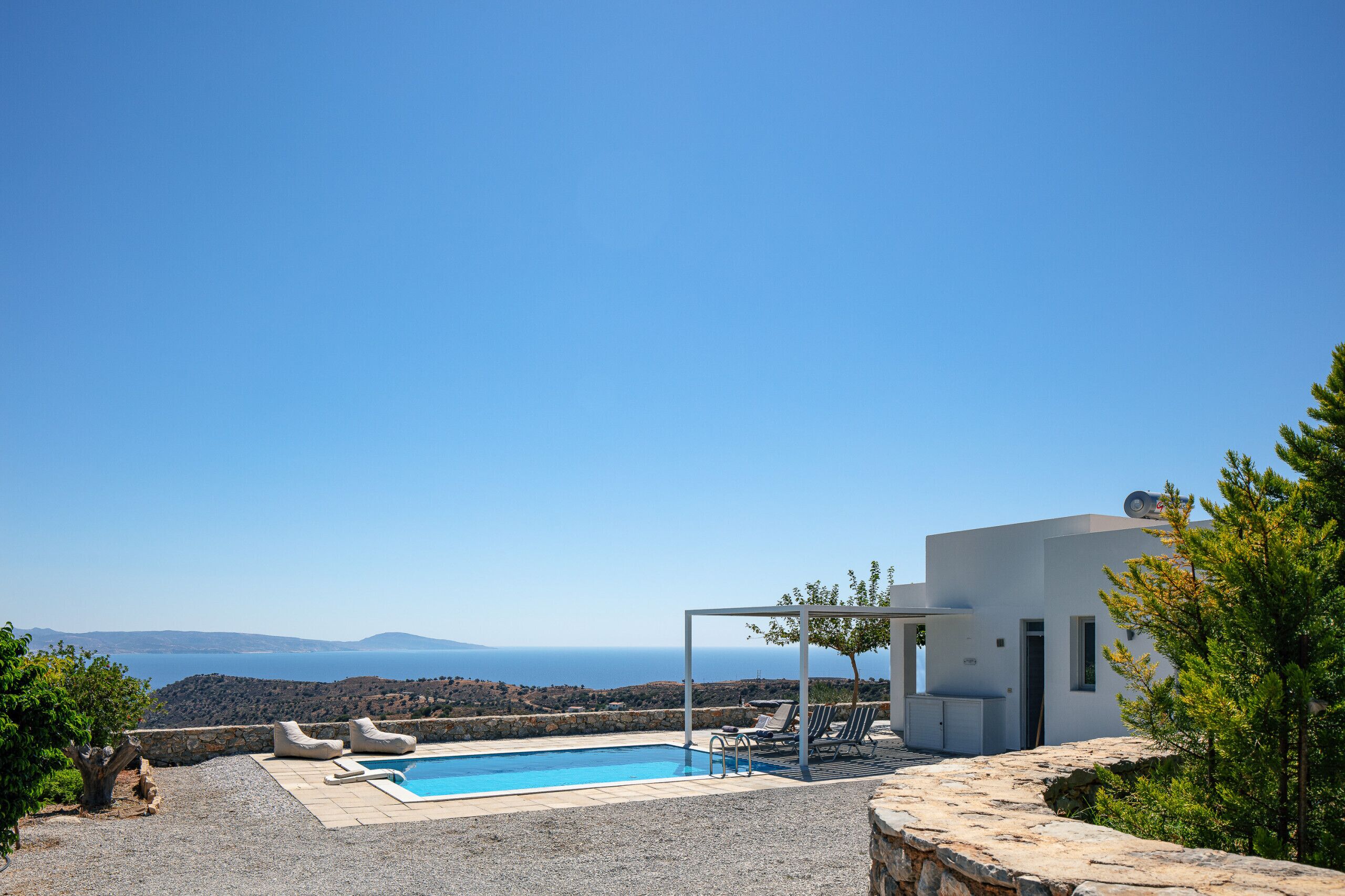 A modern outdoor pool area with a clear view of the sea and hills.