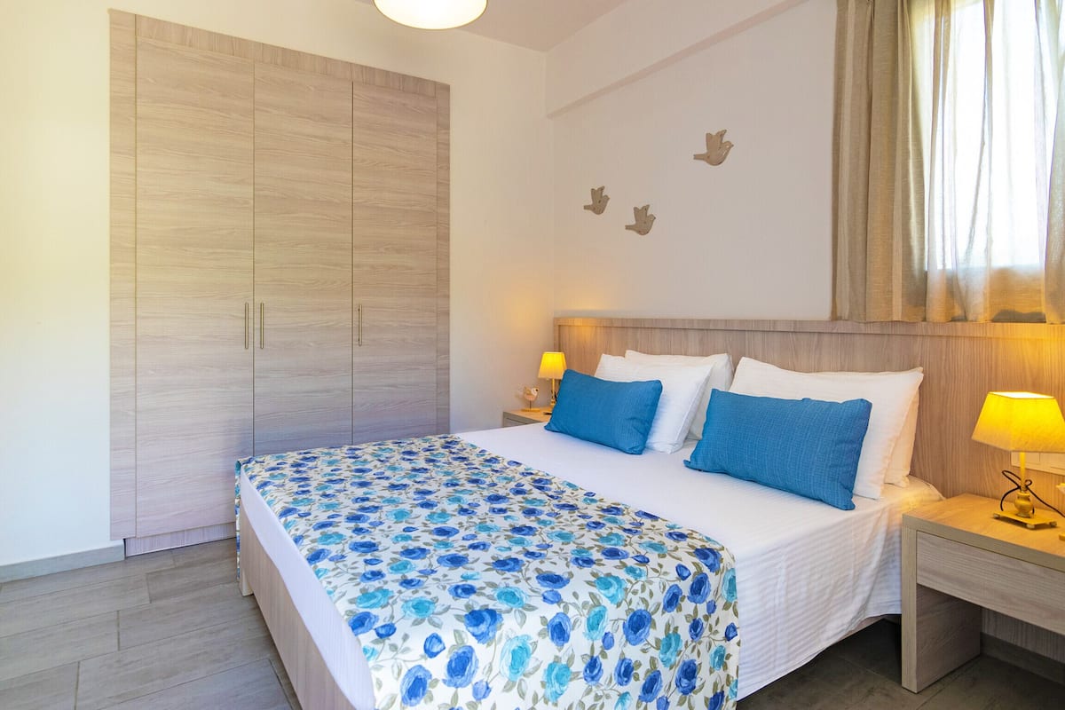 A bedroom with a large wardrobe, a bed with blue floral bedding, and a nightstand with a lamp.