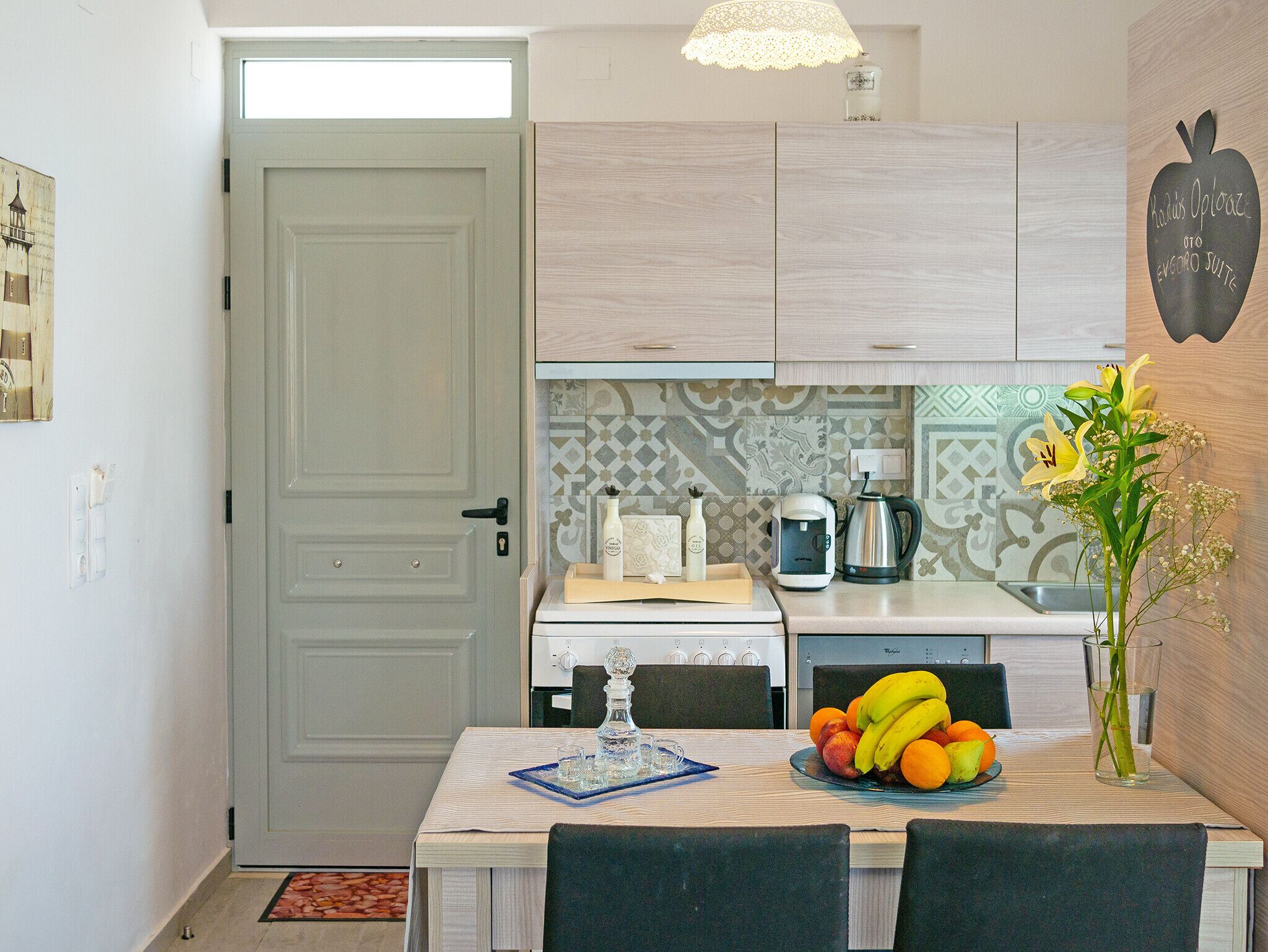 A compact kitchen with a dining area, featuring a coffee maker, a kettle, and a fruit bowl on the counter.
