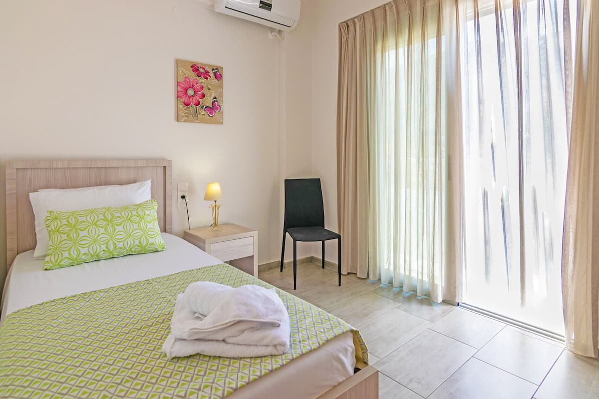 A hotel room with a bed, a chair, a nightstand, a lamp, and a window with curtains.