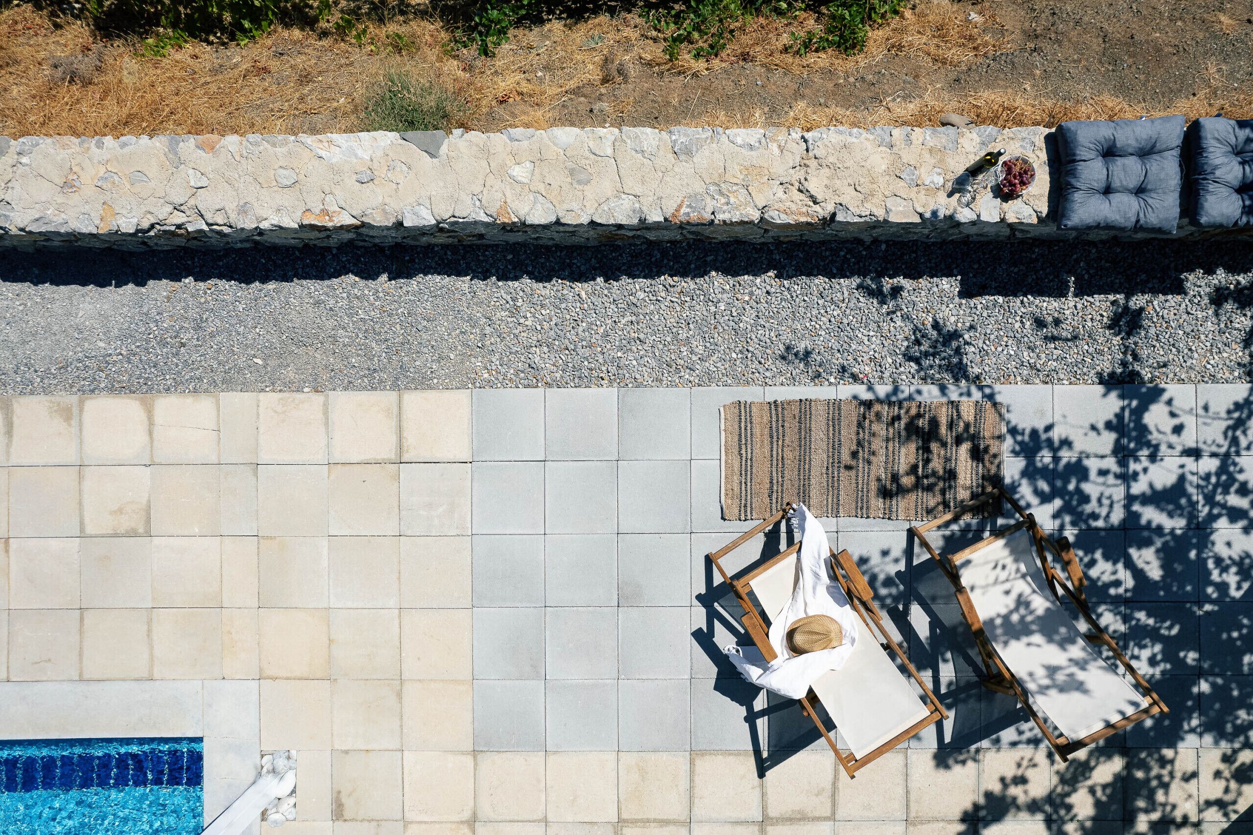 Vista aérea de un área de piscina con suelo de baldosas, pared de piedra y sillas de descanso.