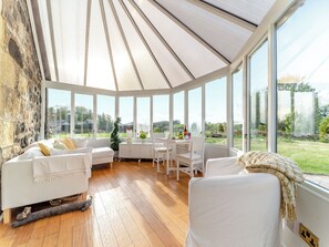 A conservatory with a stone wall, white furniture, and a view of the countryside.