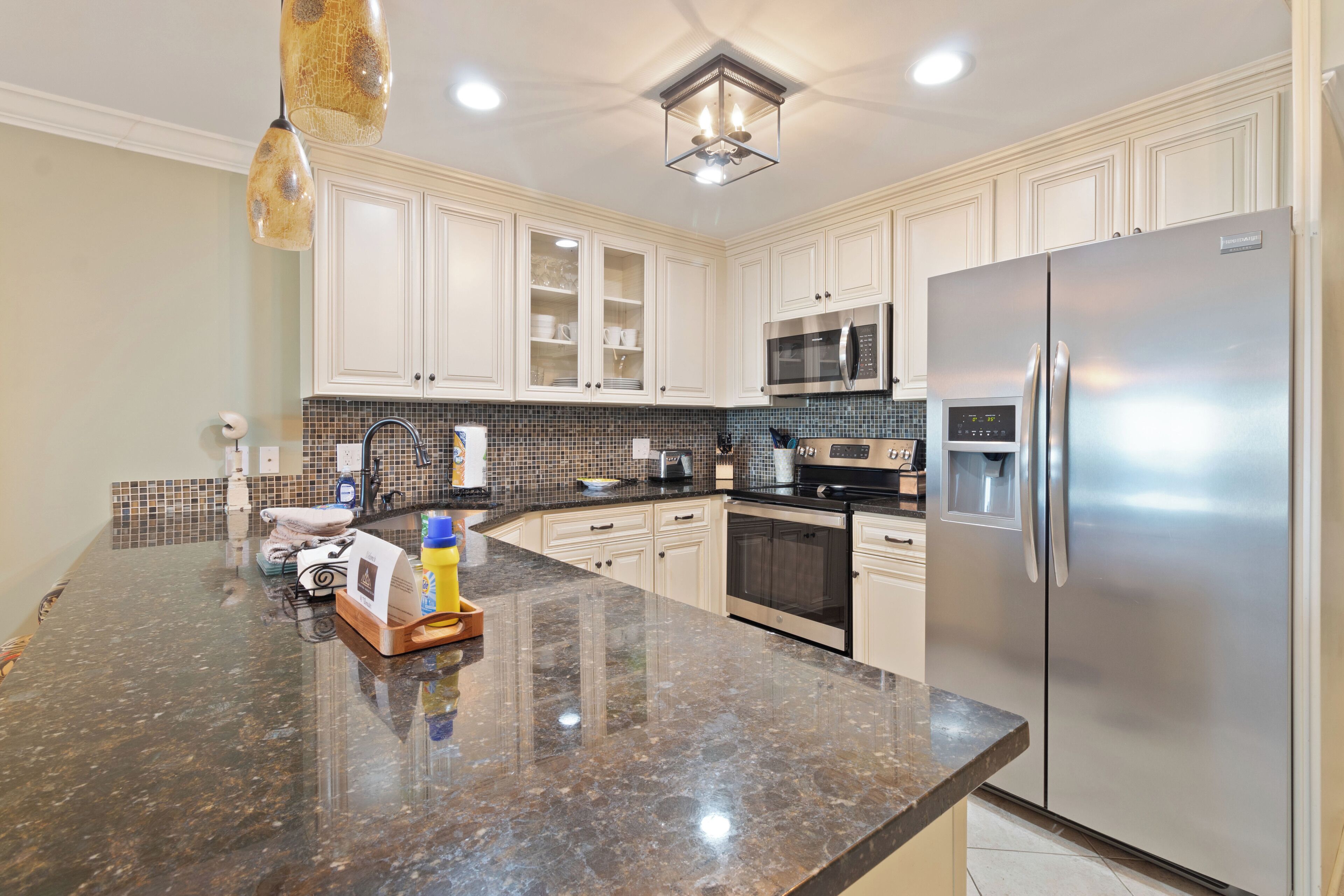 A modern kitchen with white cabinets, a stainless steel refrigerator, a microwave, and a granite countertop.
