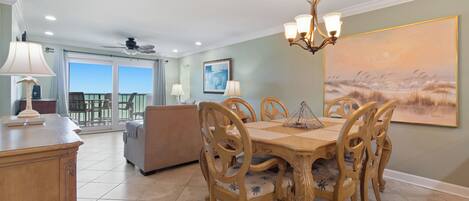 A dining area with a wooden table and chairs, a chandelier, and a large painting on the wall.