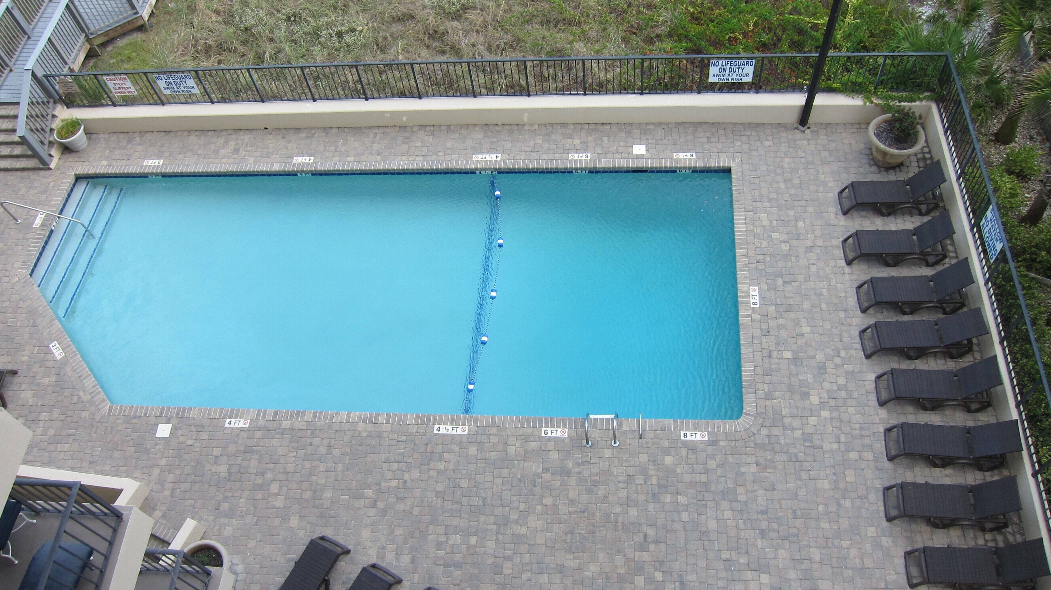 A rectangular swimming pool with a diving board, surrounded by lounge chairs and a brick deck.