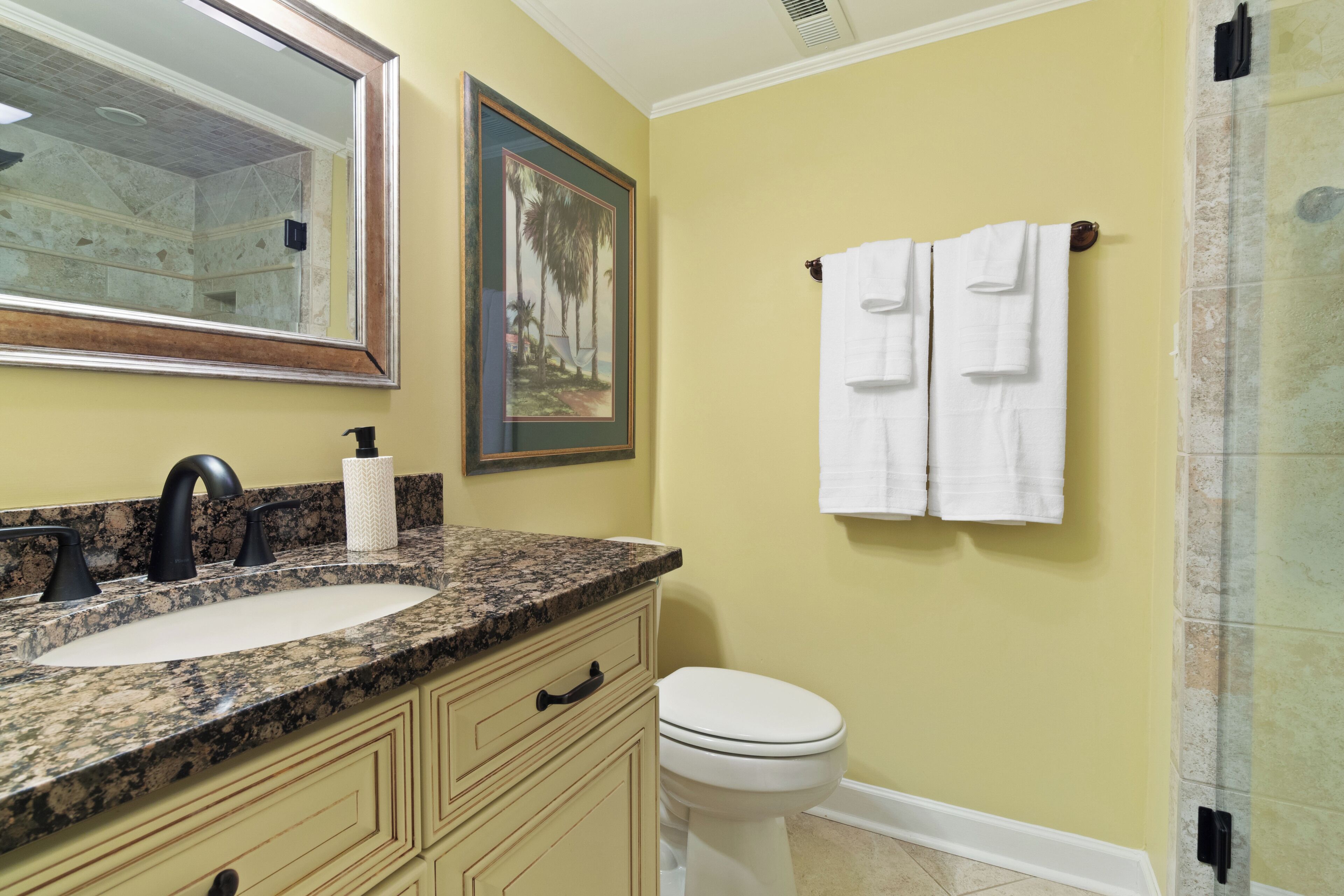 A bathroom with a granite countertop sink, a toilet, and a shower with glass doors.