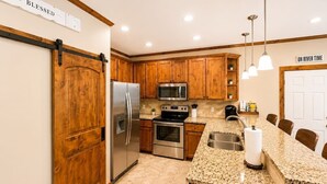 A kitchen with wooden cabinets, stainless steel appliances, a granite countertop, and a sliding barn door. - Paraiso Del Rio | 3BDRM | Guadalupe River (New Braunfels)