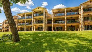 A multi-story hotel with balconies, a grassy lawn, and a bench. - Paraiso Del Rio | 3BDRM | Guadalupe River (New Braunfels)