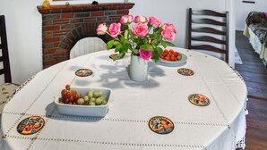 Une table à manger recouverte d’une nappe blanche, un vase rempli de roses roses, un bol de raisins et une assiette de fraises.