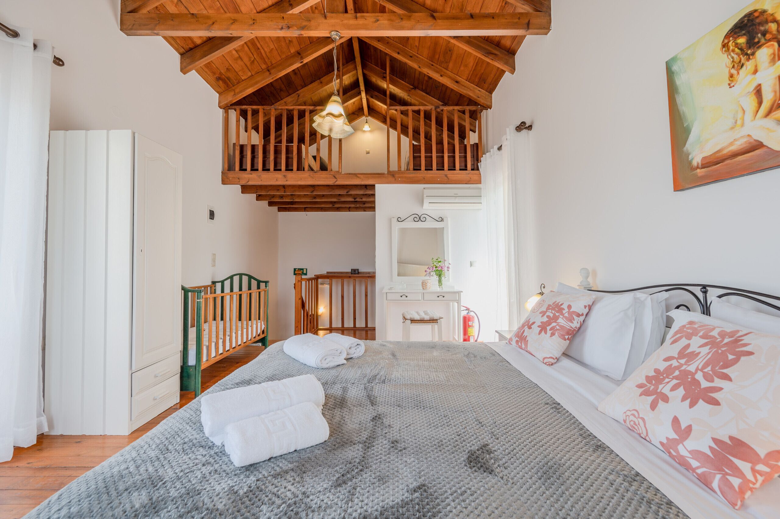 A bedroom with a wooden ceiling, a bed with floral pillows, a nightstand, a dresser, and a mirror.