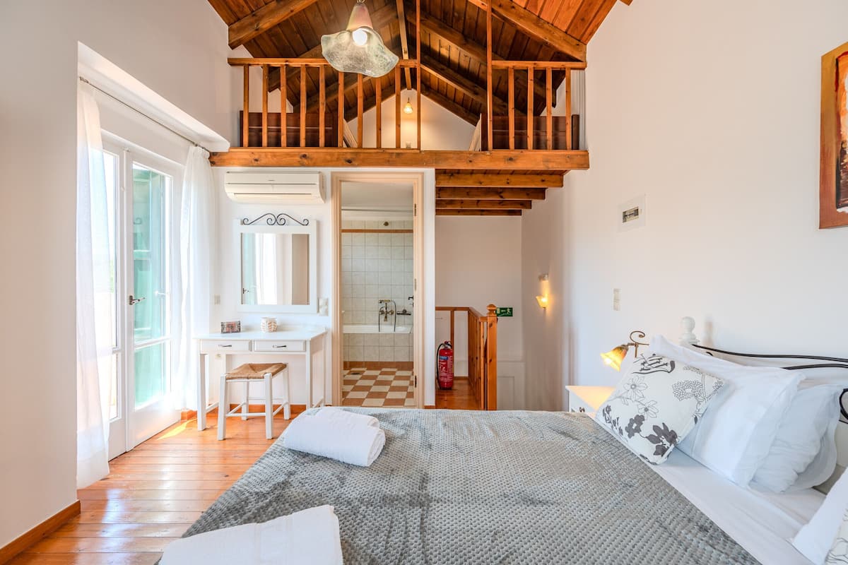A bedroom with a bed, a desk, a bathroom, and a staircase.