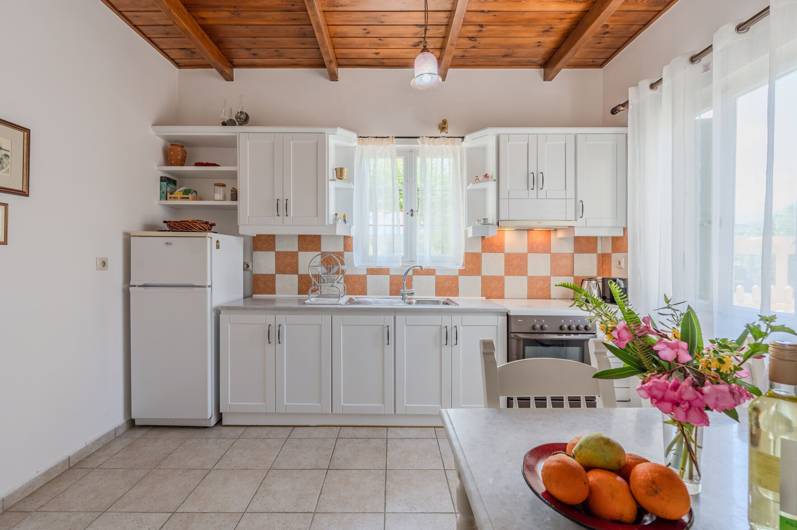 Eine kompakte Küche mit weißen Schränken, einer gefliesten Spritzschutzwand, einem Kühlschrank, einer Spüle und einem Essbereich mit Tisch und Stühlen.