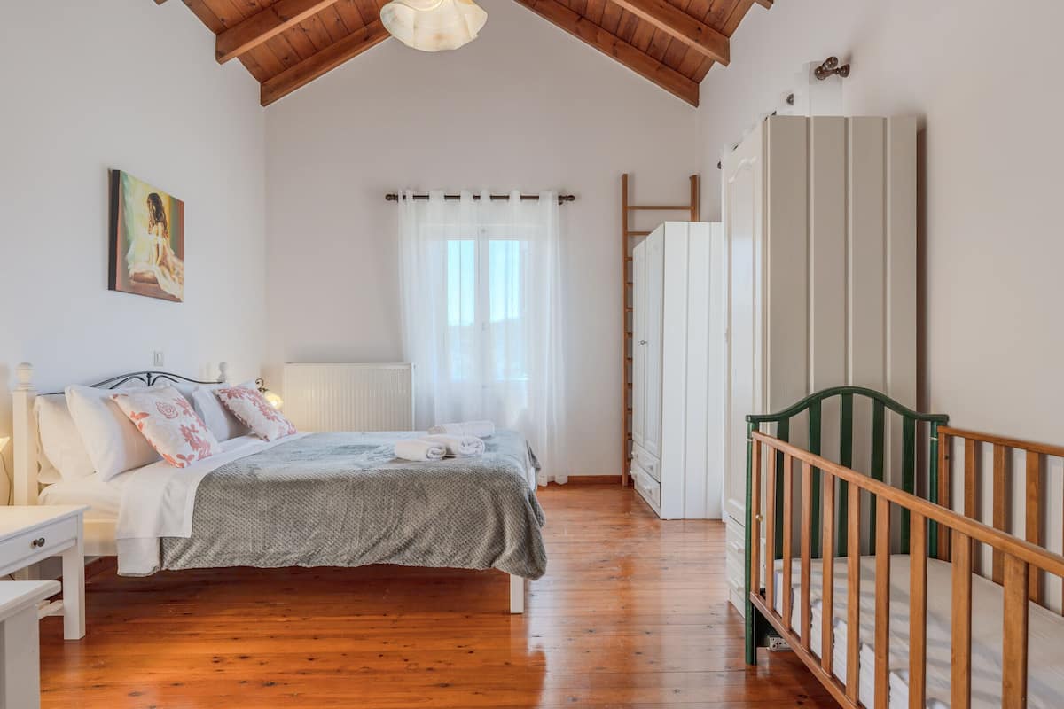 A bedroom with a wooden floor, a bed with a grey bedspread, a white radiator, and a green crib.