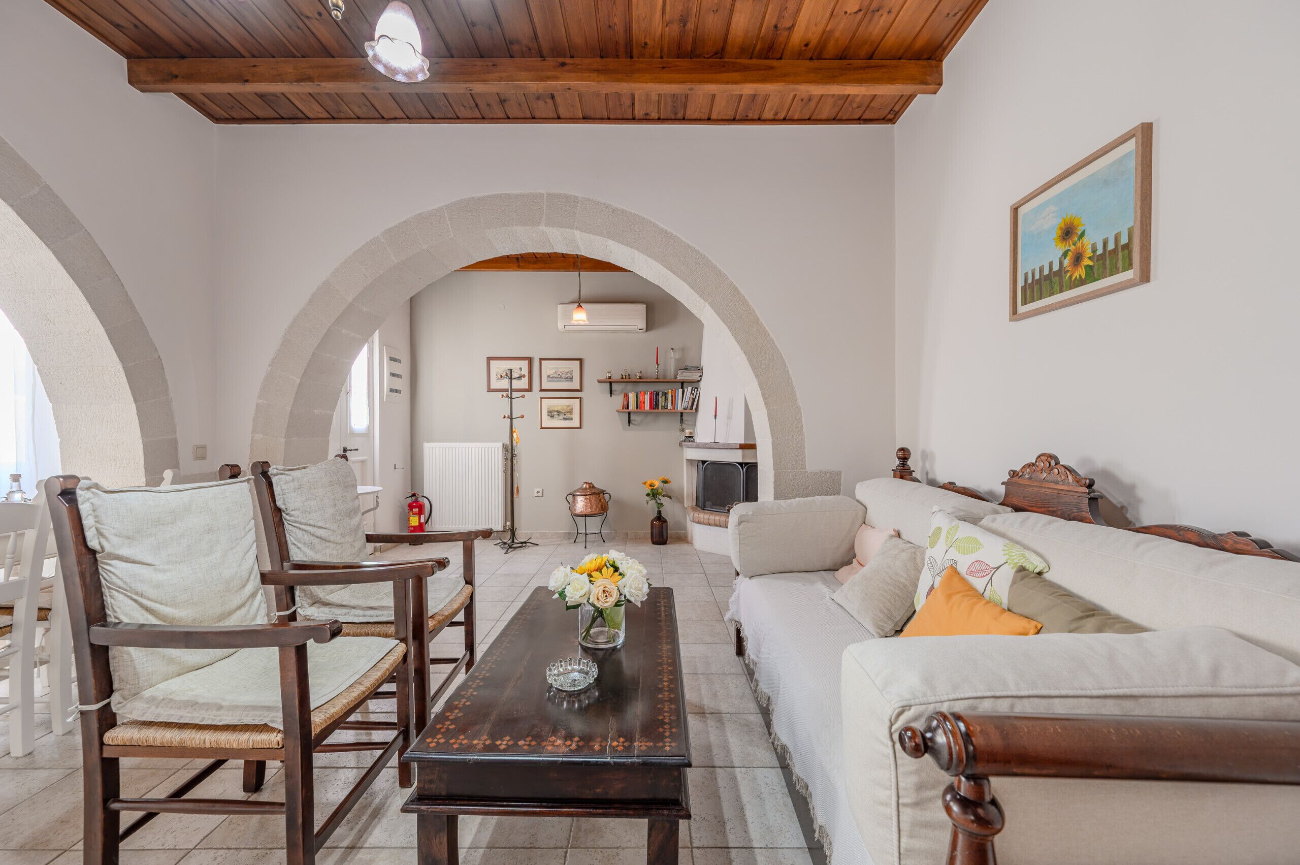 A cozy living room with a wooden ceiling, a white sofa, a wooden coffee table, and a fireplace.